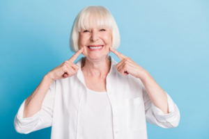 Older woman smiling on blue background and pointing to her smile