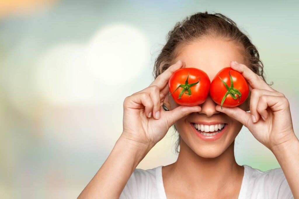 A woman holding tomatoes over her eyes